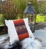 Handmade cushion cover in white with Moroccan pattern in red shades on top of plaid