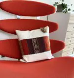 Handgemaakte kussenhoes in wit met een Marokkaans patroon in roodtinten bovenop een fauteuil