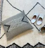 Housse de coussin marocaine faite à la main avec motif noir et blanc, sur le tapis beni ouarain avec des pantoufles blanches à côté