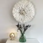 Moroccan hand-blown vase with flowers in it with table lamp and feather decoration next to it