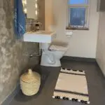 Tapis de bain marocain tissé à la main en blanc avec deux rayures noires avec pompons blancs et noirs, posé sur le sol de la salle de bain devant le lavabo