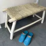 Moroccan handmade wooden bench with wicker raffia seat, standing in entrance hall, with slippers in front