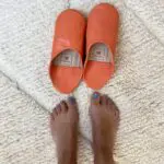 Marokkanske håndlavede slippers i orange med fodmodel ved siden af