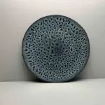 Moroccan handmade stoneware plate in green with leopard spot pattern, standing up from a wall