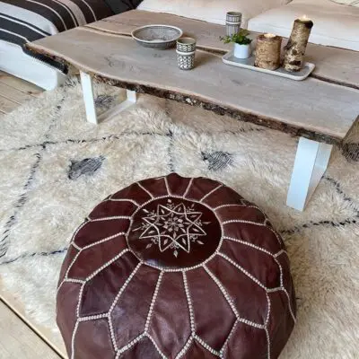 Brown leather pouf with embroidered pattern in white in a living room