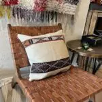 Handwoven vintage kilim montagne cushion cover in beige with Moroccan pattern in black, red and white standing on lounge chair with table next to it
