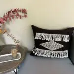 Moroccan handwoven cushion cover in black with white pattern and white tassels, standing on the corner of a sofa