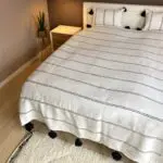 White Moroccan handwoven bedspread with black stripes and black pompoms on bed with matching pillows