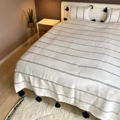 Couvre-lit marocain blanc tissé à la main avec rayures noires et pompons noirs sur le lit avec oreillers assortis