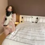 White Moroccan handwoven bedspread with black stripes and black pom poms on bed, with matching pillows and a model holding a dog