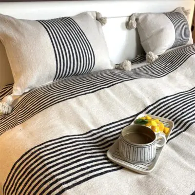 White Moroccan handwoven bedspread with black stripes and white pompoms, with breakfast dish