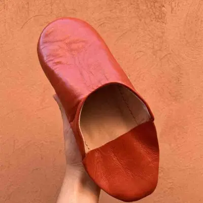Moroccan handmade slippers in terracotta, with orange wall behind