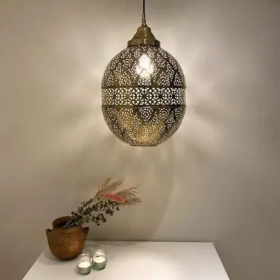 Grote handgemaakte nachtlamp van goud metaal met Marokkaans patroon, hangend boven de boekenkast met versieringen erop