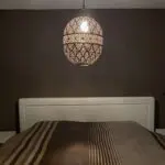 Large handmade night lamp in gold metal with Moroccan pattern, hanging above a bed