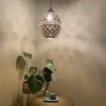 Grote handgemaakte nachtlamp van goud metaal met Marokkaans patroon, hangend in een hoek met decoraties eronder