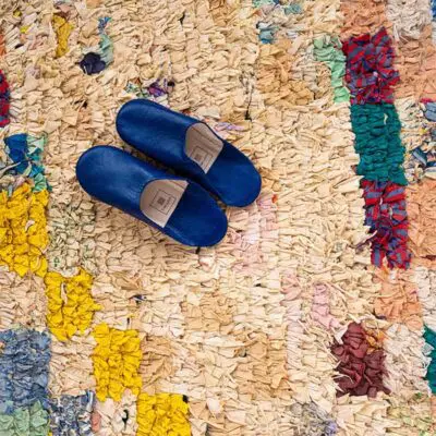 Handwoven boucherouite rug in multicolored pattern with beige tones, with midnight blue slippers on top, dense