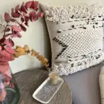 Moroccan handwoven cushion cover in beige with wool details on the sides, with a black stripe pattern, sitting on a sofa corner