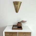 Applique artisanale en métal doré à motif marocain accrochée sur un mur blanc avec une étagère en dessous