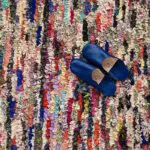 Marokkaans handgeweven Boucherouite-tapijt in veelkleurig patroon met blauwe pantoffels erop