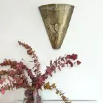 Handmade wall lamp in gold metal with a Moroccan pattern, which hangs above a vase with red flowers in it