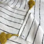 White Moroccan handwoven bedspread with black stripes and yellow pompoms