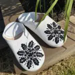 Moroccan handmade slippers in white with black sequins, outside by a flower bed