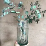 Kleine handgefertigte transparente Beldi-Vase mit grünen Blumen darin