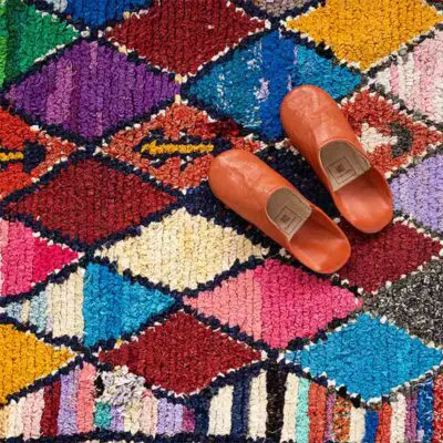 Handwoven boucherouite rug in multicolored diamond pattern, with orange slippers on top