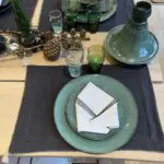 Kolgrå marockanska handbroderade bordstabletter med vit bård och vita pomponger på ett fint dukat bord med stengodsservice och beldiglas