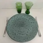 Moroccan handmade stoneware plate in green with leopard spot pattern, with knife and fork, and green beldi glass and wine glass next to it