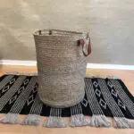Moroccan handwoven basket with leather handle standing on carpet