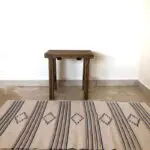 Handwoven beige cotton rug with Moroccan roots and stripes pattern, in front of a footstool