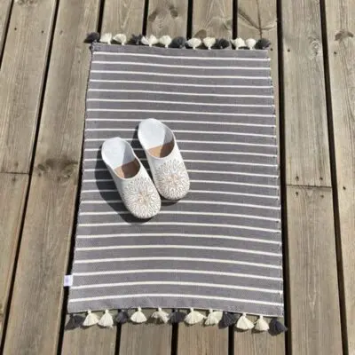 Moroccan handmade bath mat in gray with slippers on top, outside