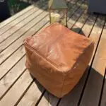 Moroccan handmade square leather pouf in light brown, standing on pavilion outside