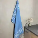 Moroccan handwoven hammam towel in blue hanging on a hook in a bathroom