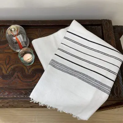 white Moroccan handmade hammam towel with black stripes, on top of shelf with glass decorations next to it