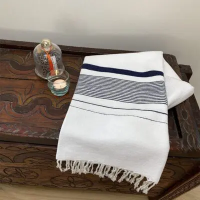 white Moroccan handmade hammam towel with dark blue stripes on shelf with glass decorations next to it