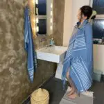 Model met Marokkaanse handgeweven hamamdoek in blauw buiten in een badkamer