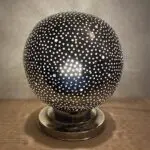Moroccan table lamp in silver metal with a single hole pattern that is lit