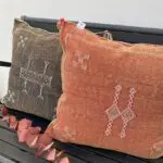 Moroccan handwoven cactus silk cushion cover in dark brown and terracotta color with white details, on a bench with decorations