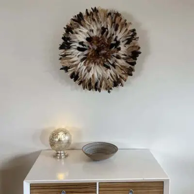 Moroccan handmade bowl in beige on a shelf, with feather decoration above and a table lamp next to it