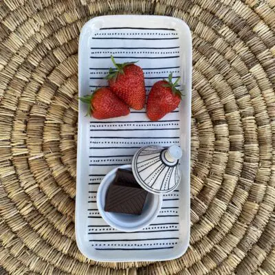 Kleine Tajine-Schale mit Punktmuster und Schokolade darin, auf einem Teller mit passendem Muster und Erdbeeren darauf