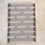 Handwoven cotton rug in white with Moroccan stripe and dot pattern in light blue with brown tassels