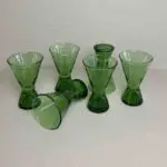 Six handmade green beldi wine glasses, one of them standing upside down and one of them lying down
