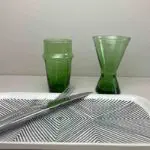 Handgjorda gröna beldiglas och vinglas som står bredvid ett fat