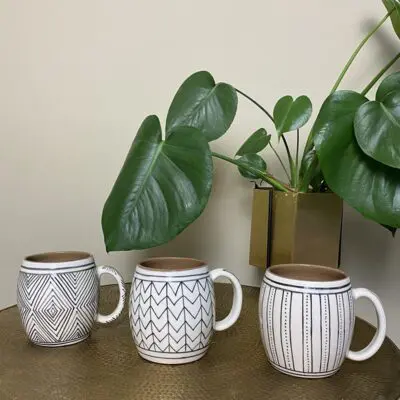 Three Moroccan handmade ceramic mugs with handles in three different patterns, such as dot pattern, zigzag pattern and ethnic chic pattern, standing on a table