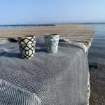 two Moroccan handmade mugs in beige with black and light blue stripe patterns standing on a bridge on top of a plaid