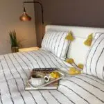 White Moroccan handwoven bedspread with black stripes and yellow pompoms, with matching pillows and breakfast dish on top