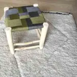 Moroccan handmade wooden stool with seat of braided cord in black and green, standing on carpet
