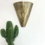 Applique artisanale en métal doré à motif marocain, suspendue à côté de cactus